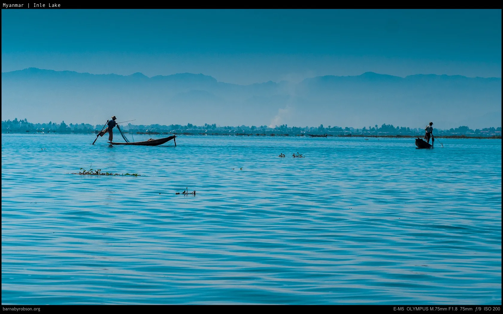 Inle Lake with two traditional leg-rowing fishermen and distant hills.
