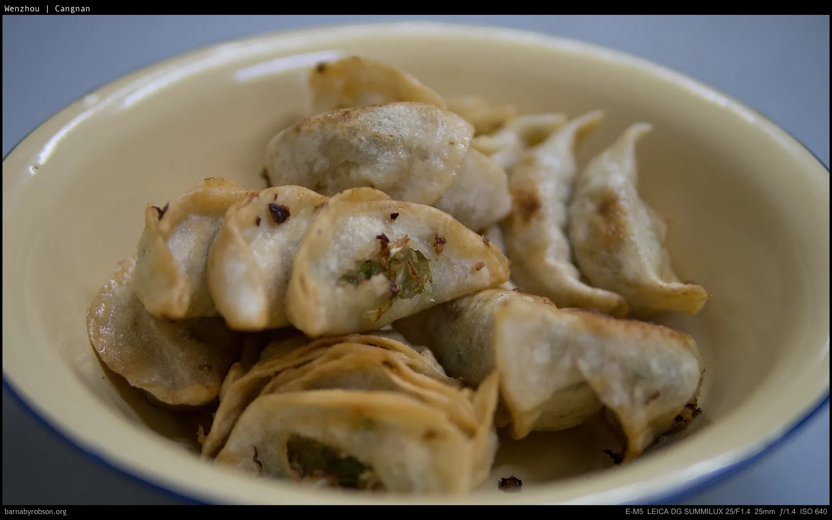 Golden pan-fried dumplings with green filling in a yellow enamel bowl.