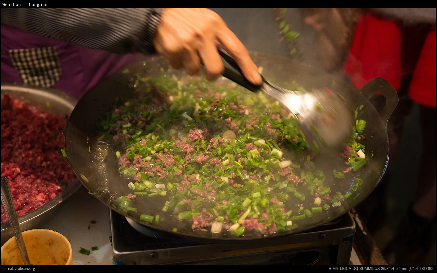 Hand stirring minced meat and spring onions in a steaming wok.