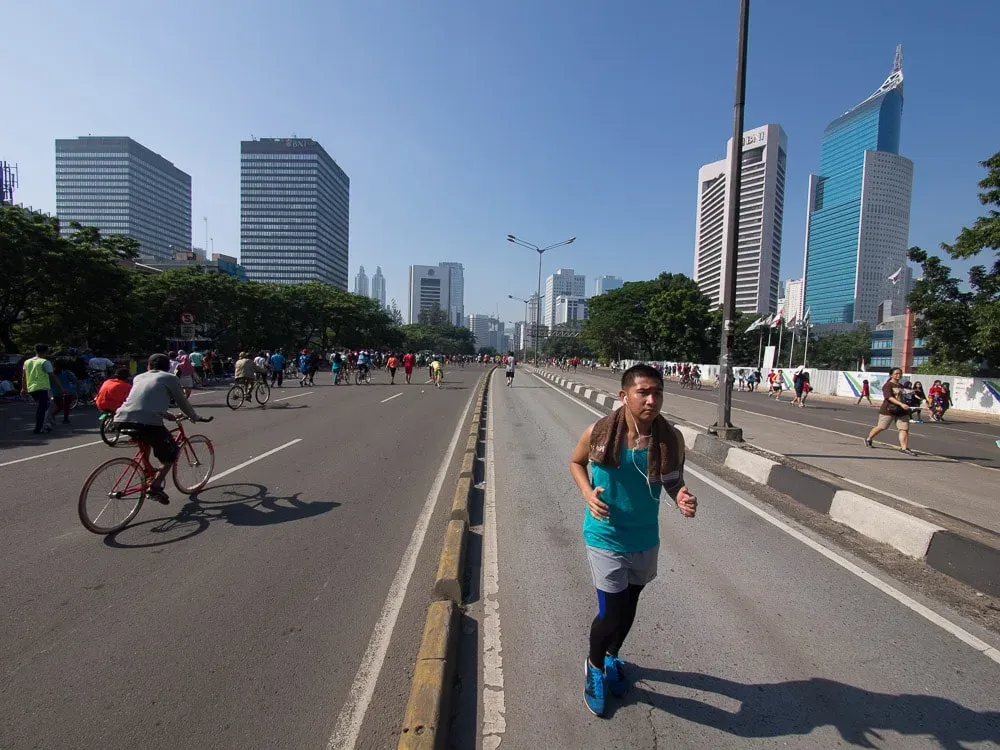 A lone cyclist on Jakarta's Sudirman boulevard during car-free day, skyscrapers behind.