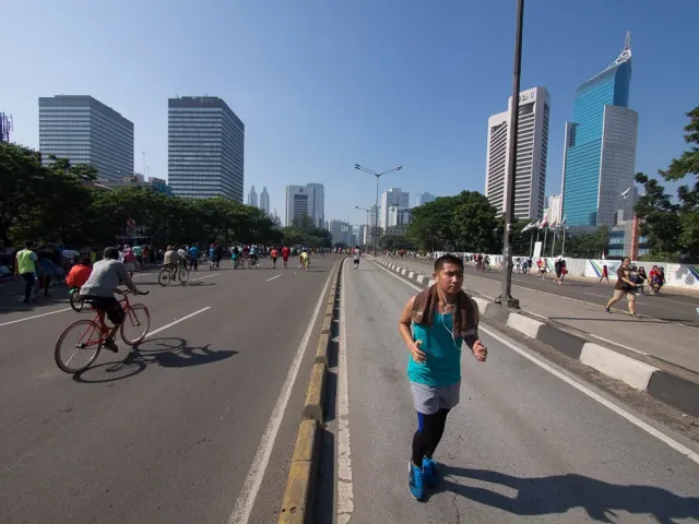 A lone cyclist on Jakarta's Sudirman boulevard during car-free day, skyscrapers behind.