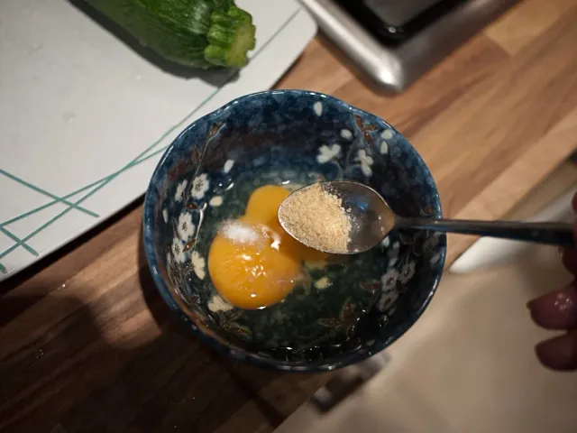 A raw egg yolk in a black bowl beside chopped tomatoes.