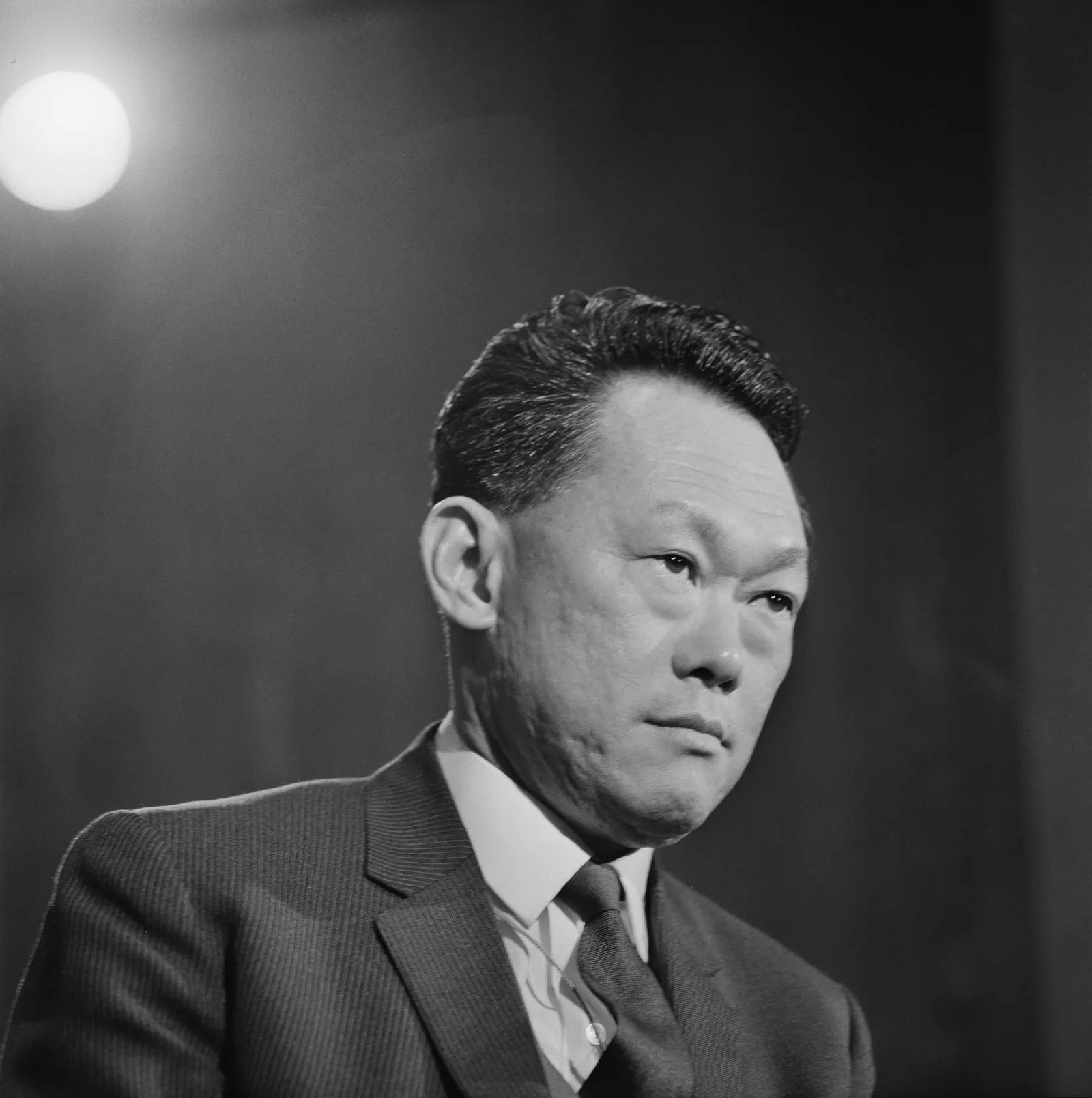 Black and white portrait of a young Lee Kuan Yew in a pinstriped suit, lit by a single studio lamp.