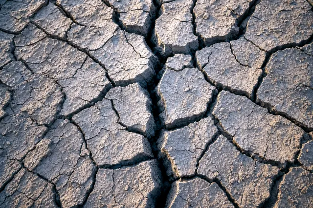 Close view of cracked, fissured dry earth splitting into fragments, evoking unstable economic foundations.