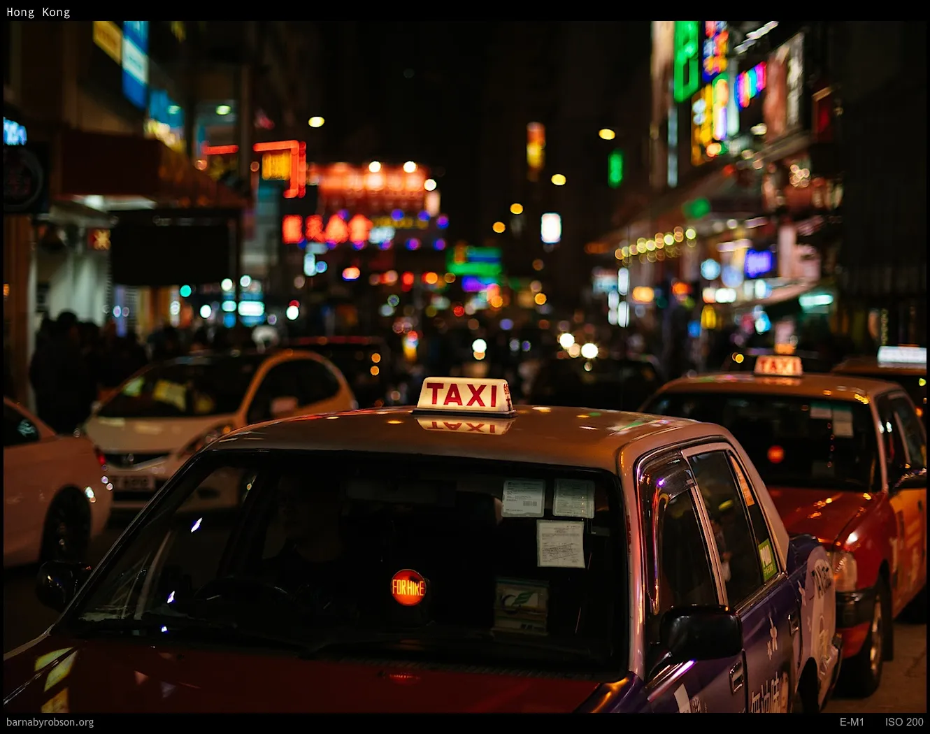 Hong Kong street at night with taxis and blurred neon signs.