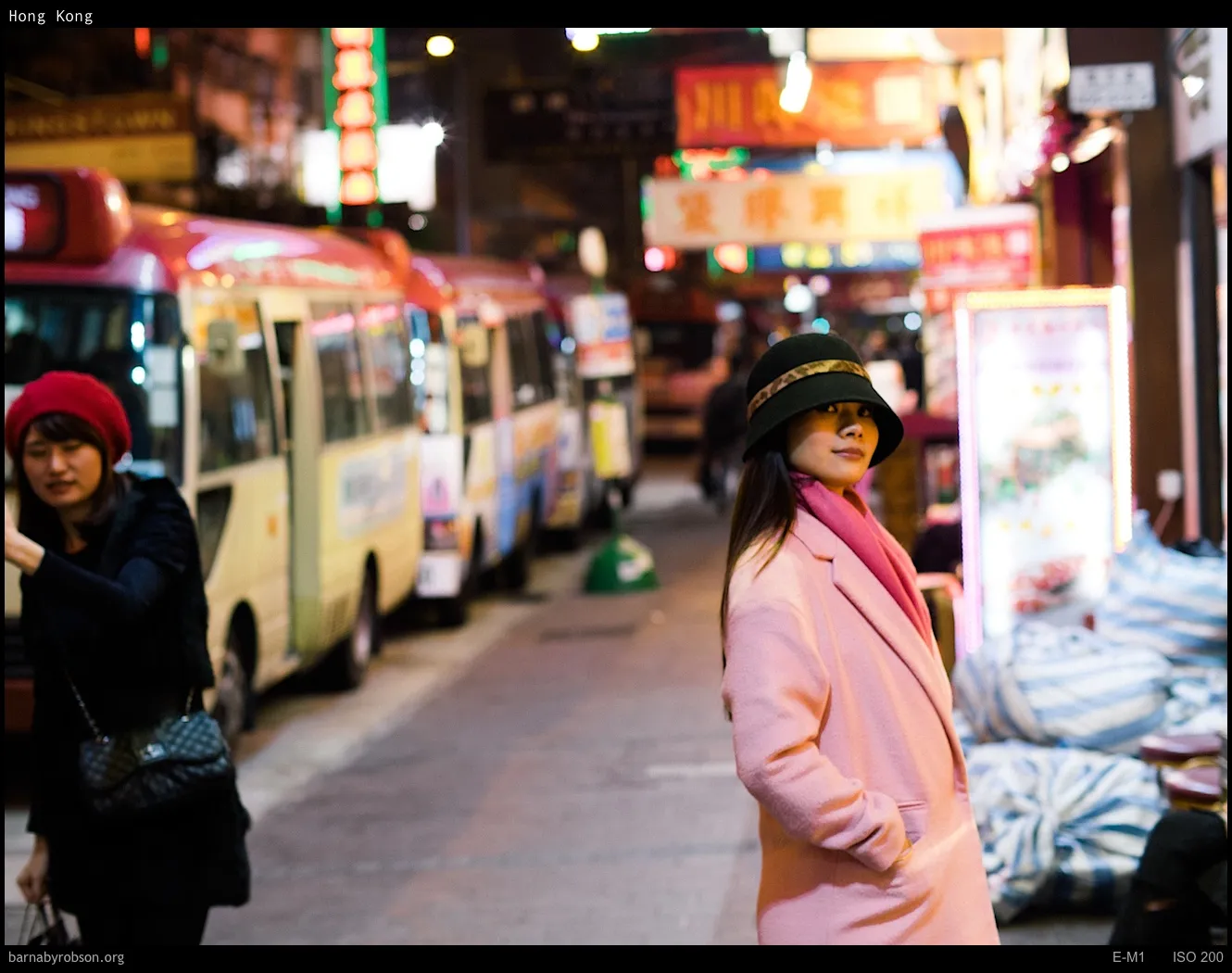 Woman in pink coat and hat on a neon-lit Hong Kong street.