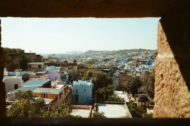 The blue city of Jodhpur seen from a shaded arch of Mehrangarh Fort, indigo houses spilling across the valley toward distant hills.