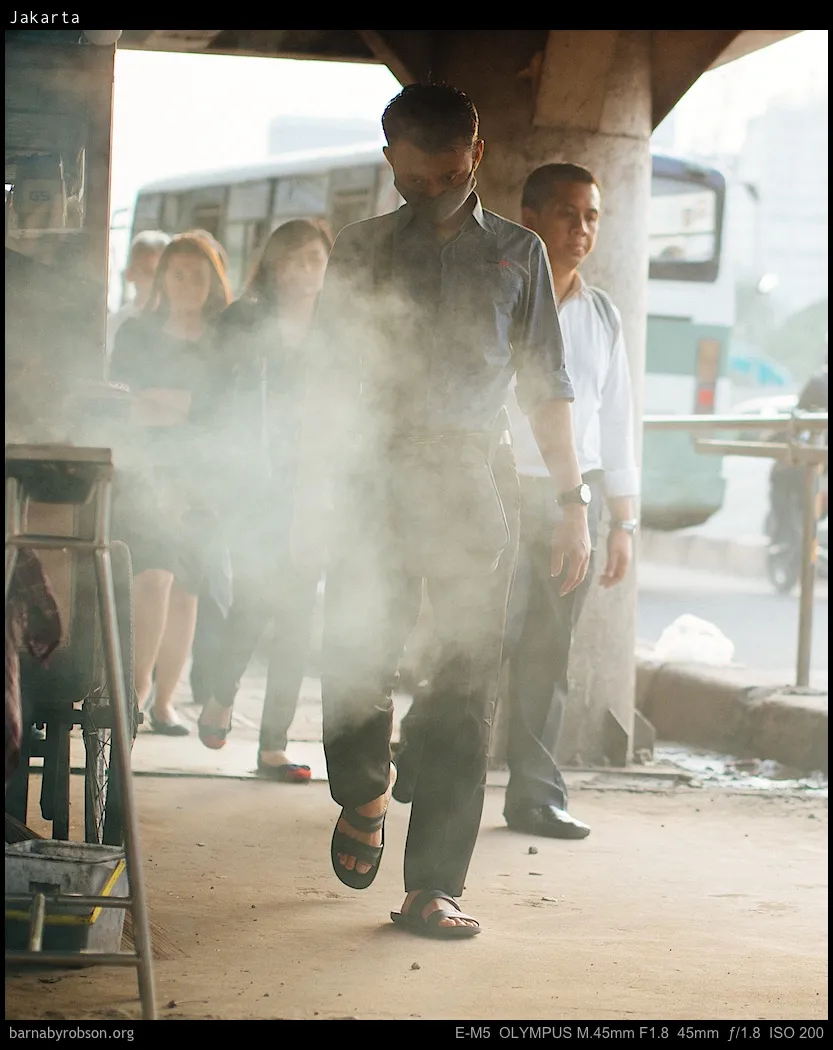 Masked man walks through smoke on a busy Jakarta street.