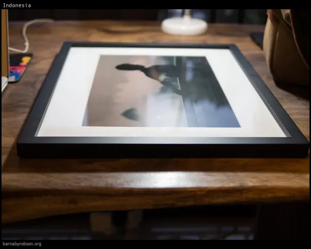A newly framed black-and-white print resting on a wooden table.