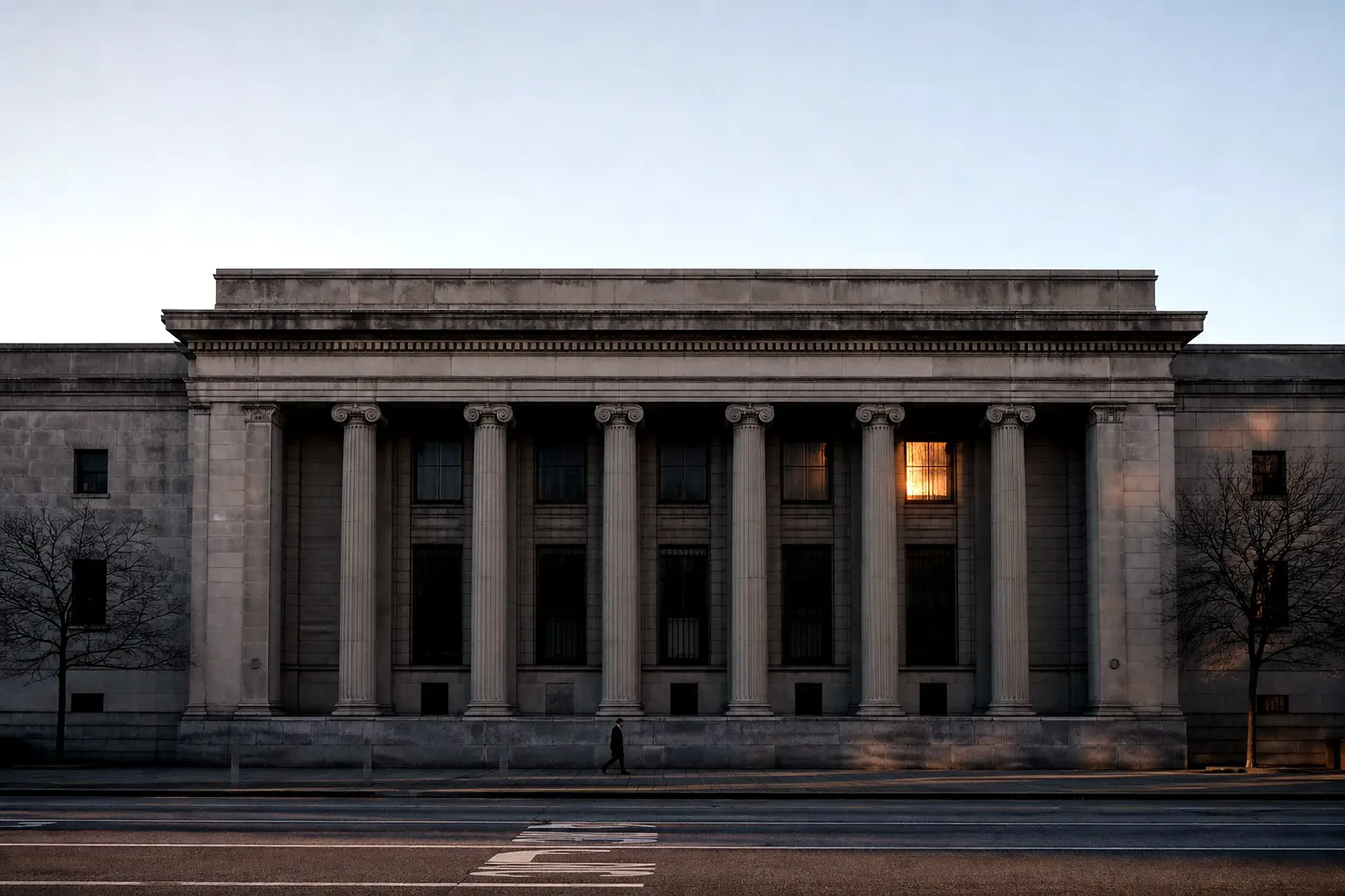 The stone facade of a grand central bank at cold dawn, one commuter passing small beneath the columns, a thin band of sunrise caught in a high window.