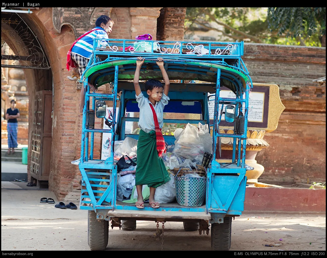 Two boys on a blue three-wheeled vehicle, one climbing, one standing.