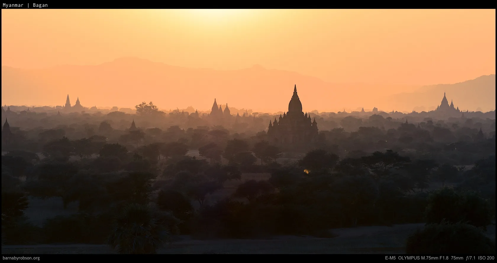Bagan temples silhouetted against an orange, misty sunrise sky.