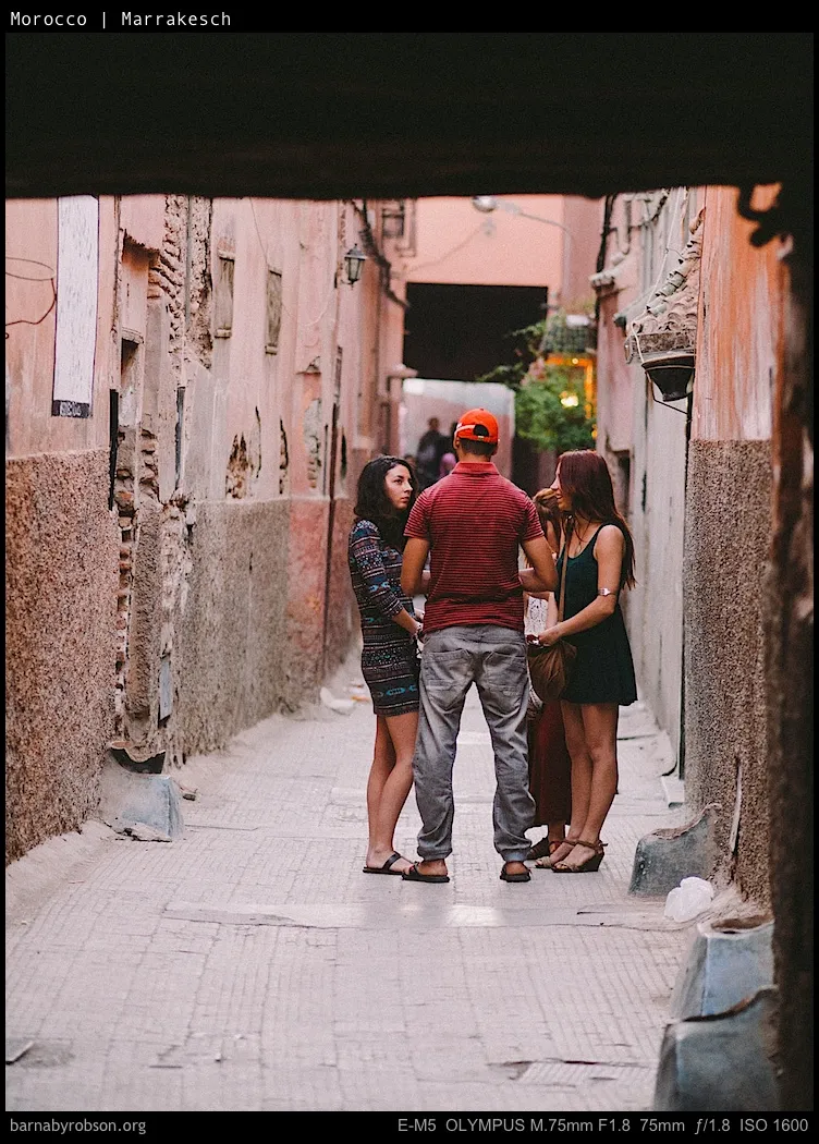Three people standing in a narrow, pink-walled alley in Marrakech.
