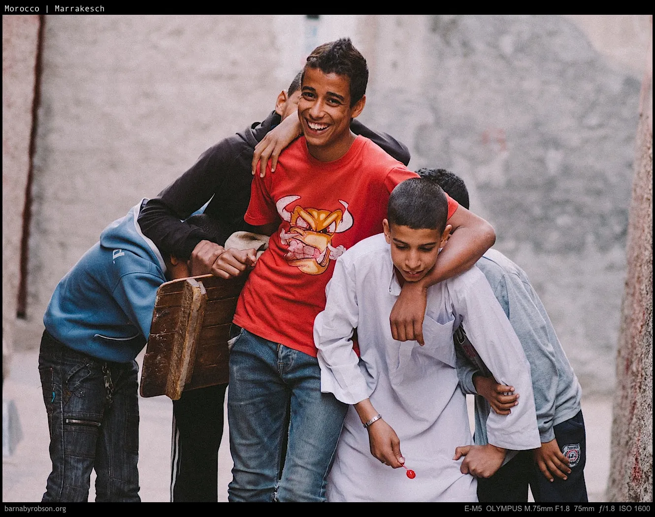 Five young boys huddle together, one smiling, another holding a red lollipop.