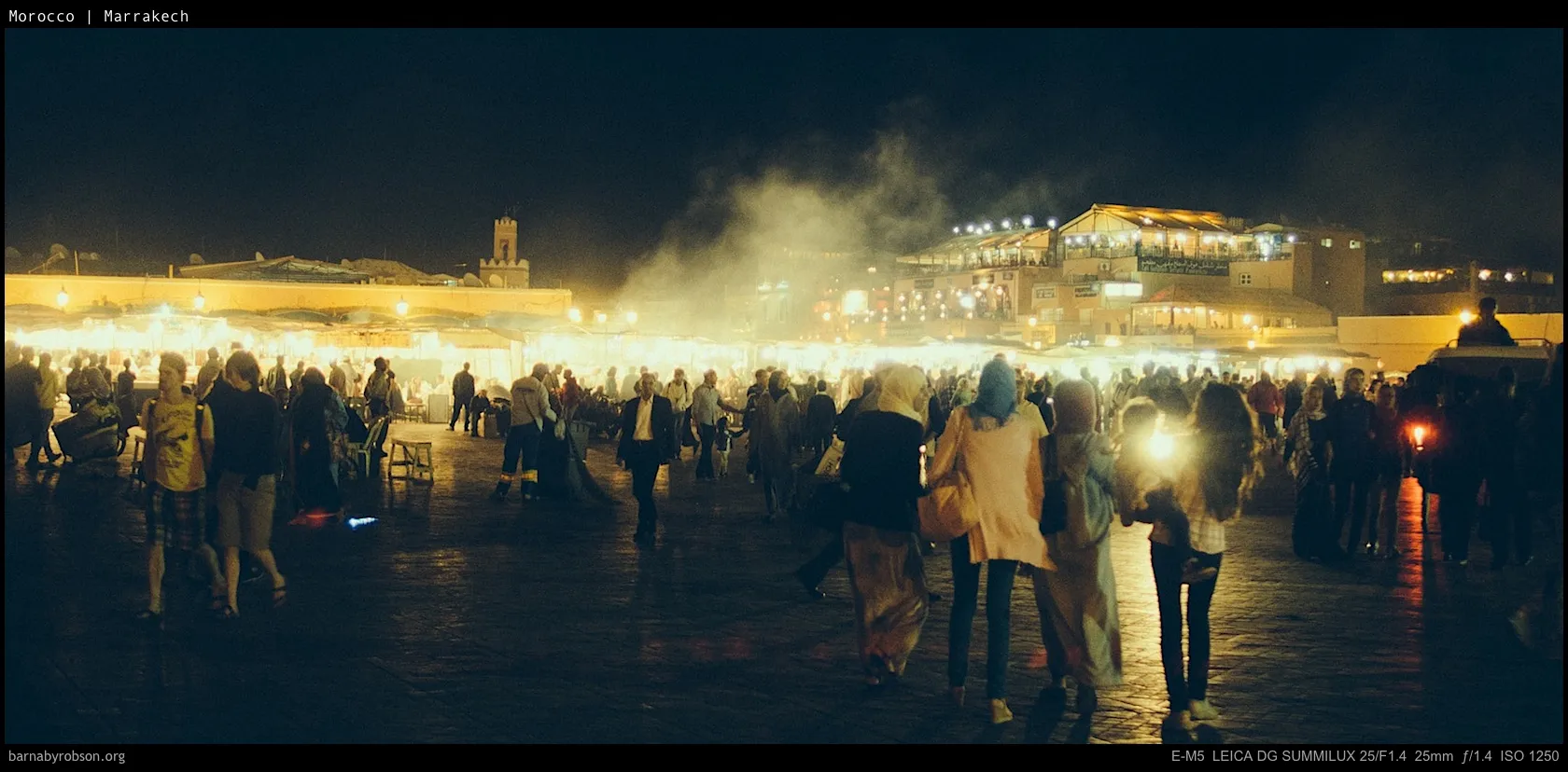 Busy Marrakech market at night, with crowds, stalls, and bright lights.
