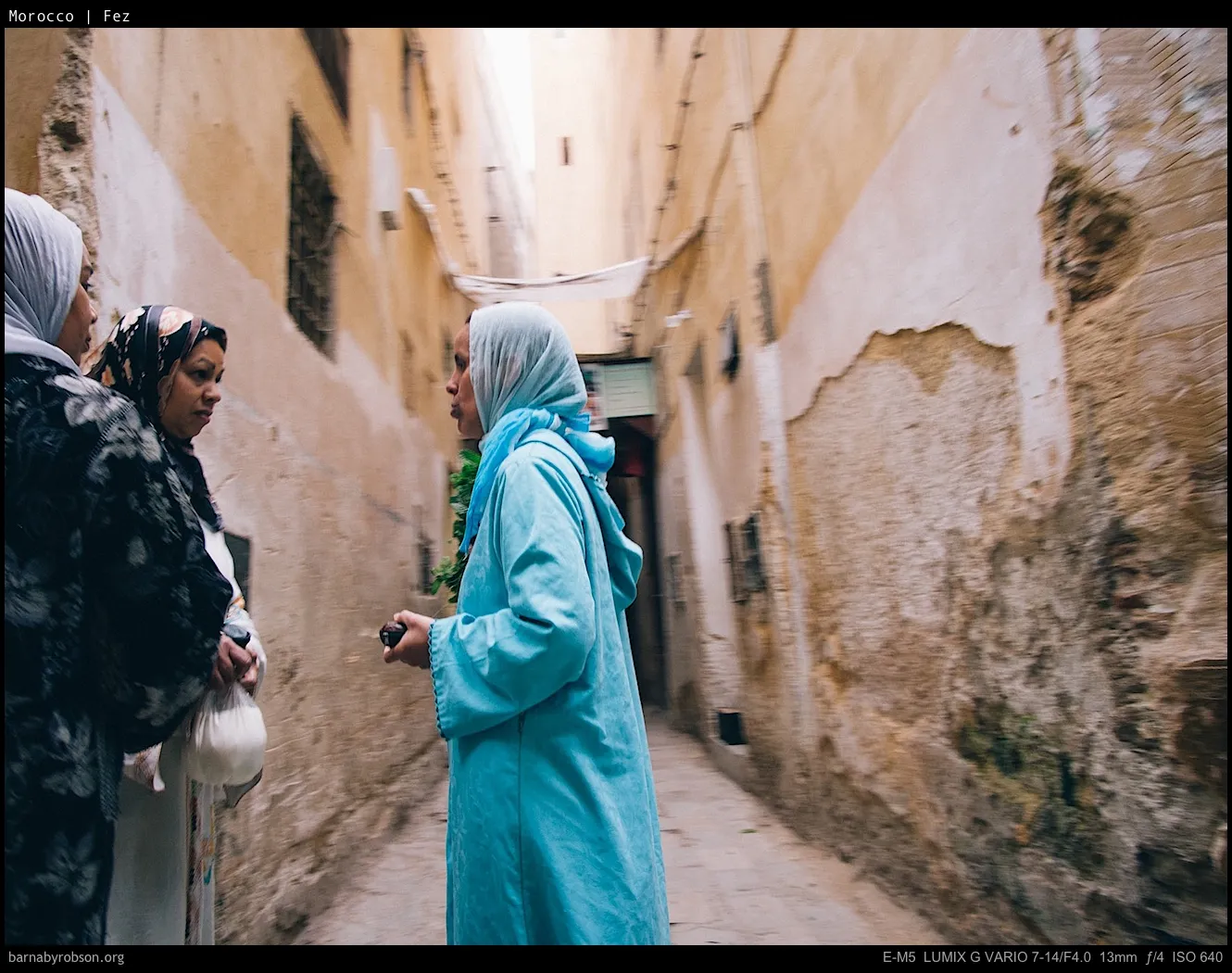 Three women in headscarves and robes in a narrow, old alley.