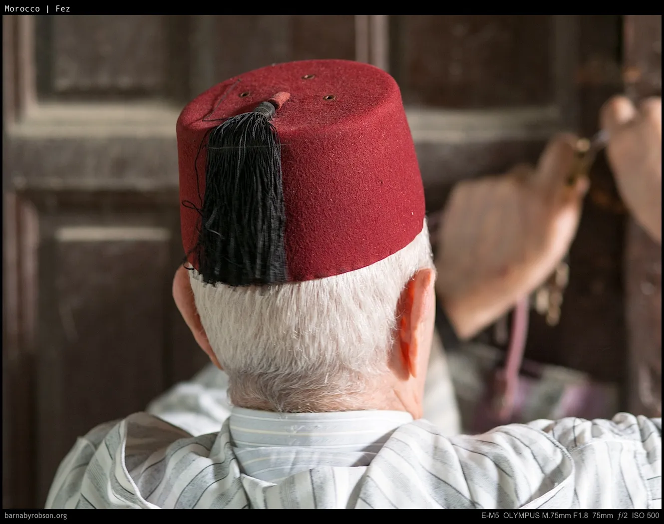 Back of an elderly person wearing a red fez, hands holding keys at a door.
