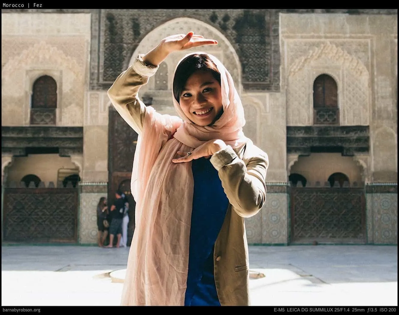 Smiling woman in pink headscarf posing before ornate Moroccan building.