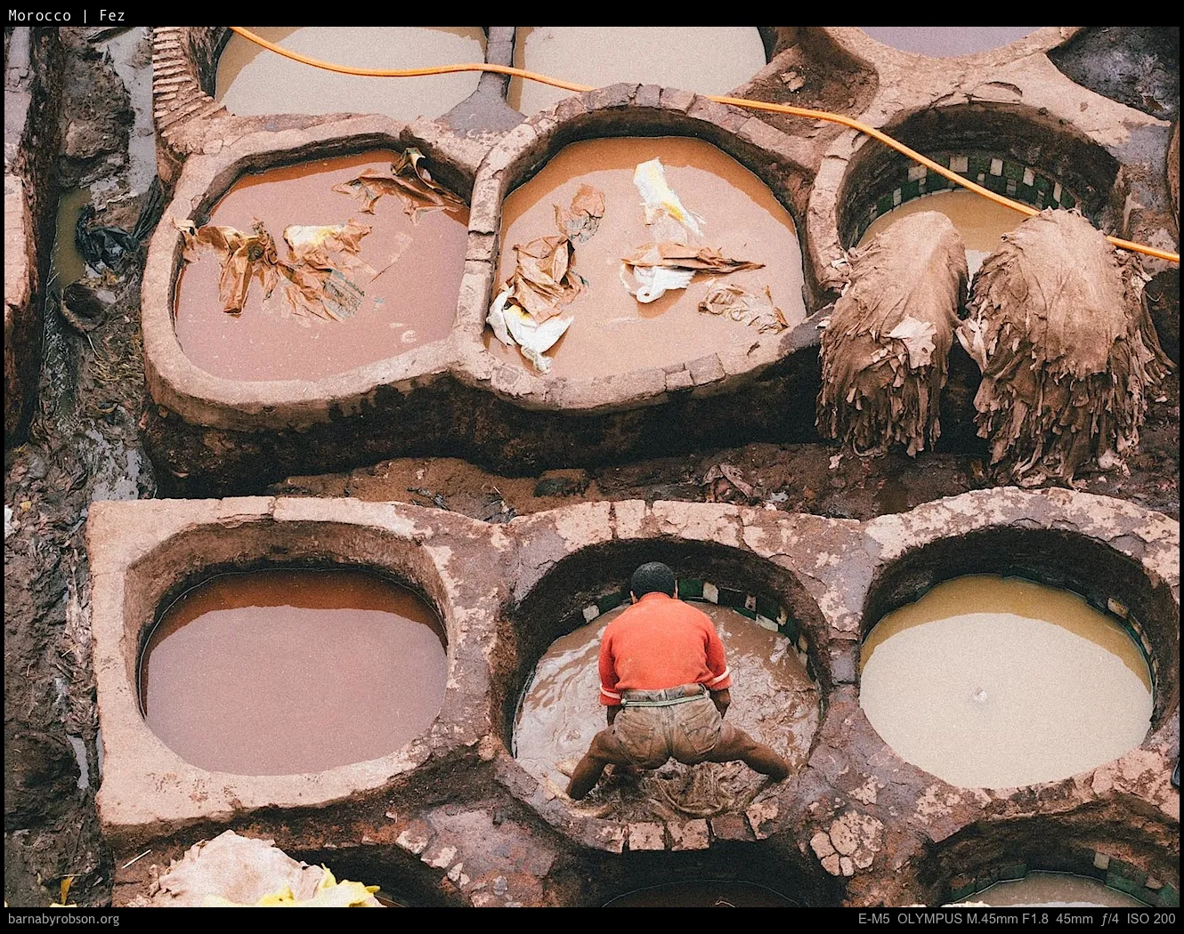 Worker in a traditional tannery vat, surrounded by hides and coloured liquids.