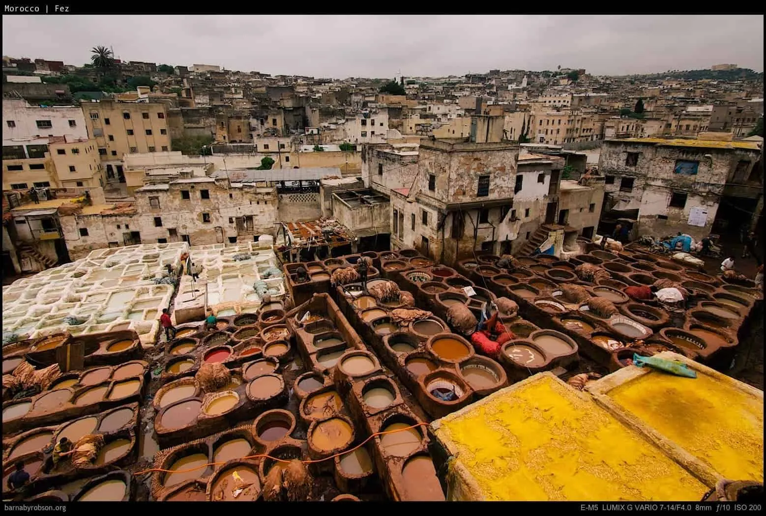 Fez tannery with numerous colourful dyeing vats, workers, and old city buildings.