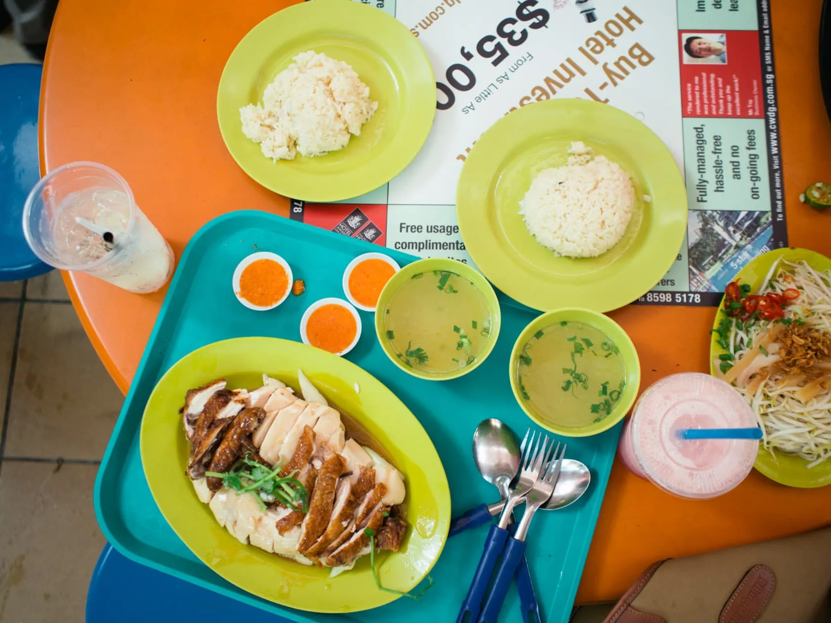 Top-down spread of Hainanese chicken rice, chilli sauces, soup and bean sprouts on hawker trays at Maxwell Food Centre