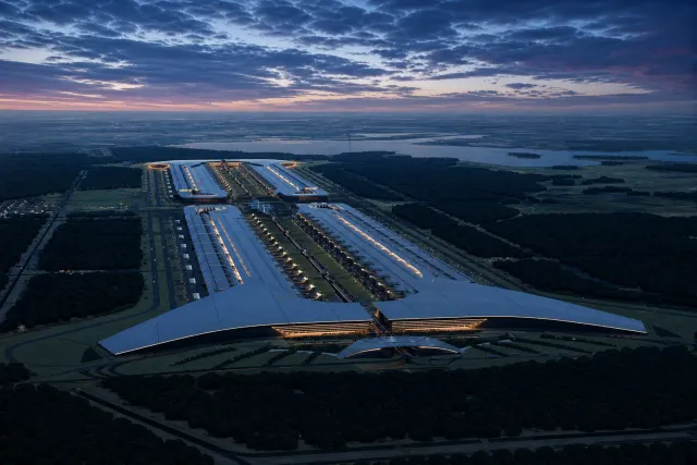 An illuminated hyperscale data-centre campus stretches through forest beneath a blue and pink dusk sky.