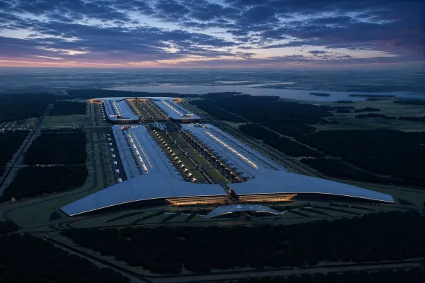 An illuminated hyperscale data-centre campus stretches through forest beneath a blue and pink dusk sky.