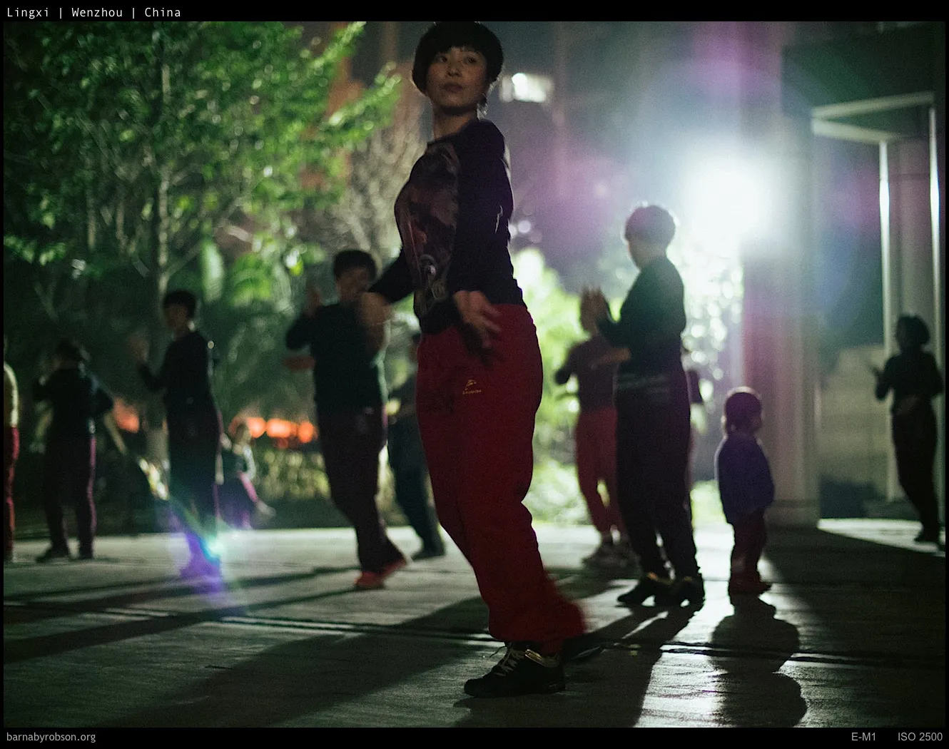 Woman in red trousers and others exercising outdoors at night.