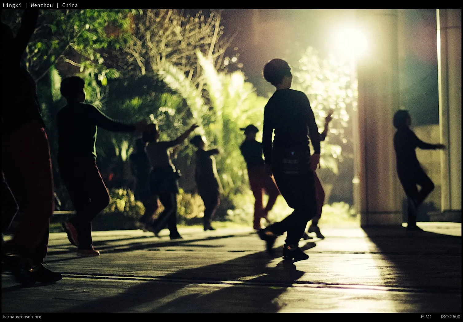 Silhouetted people dancing outdoors at night, illuminated by bright light.