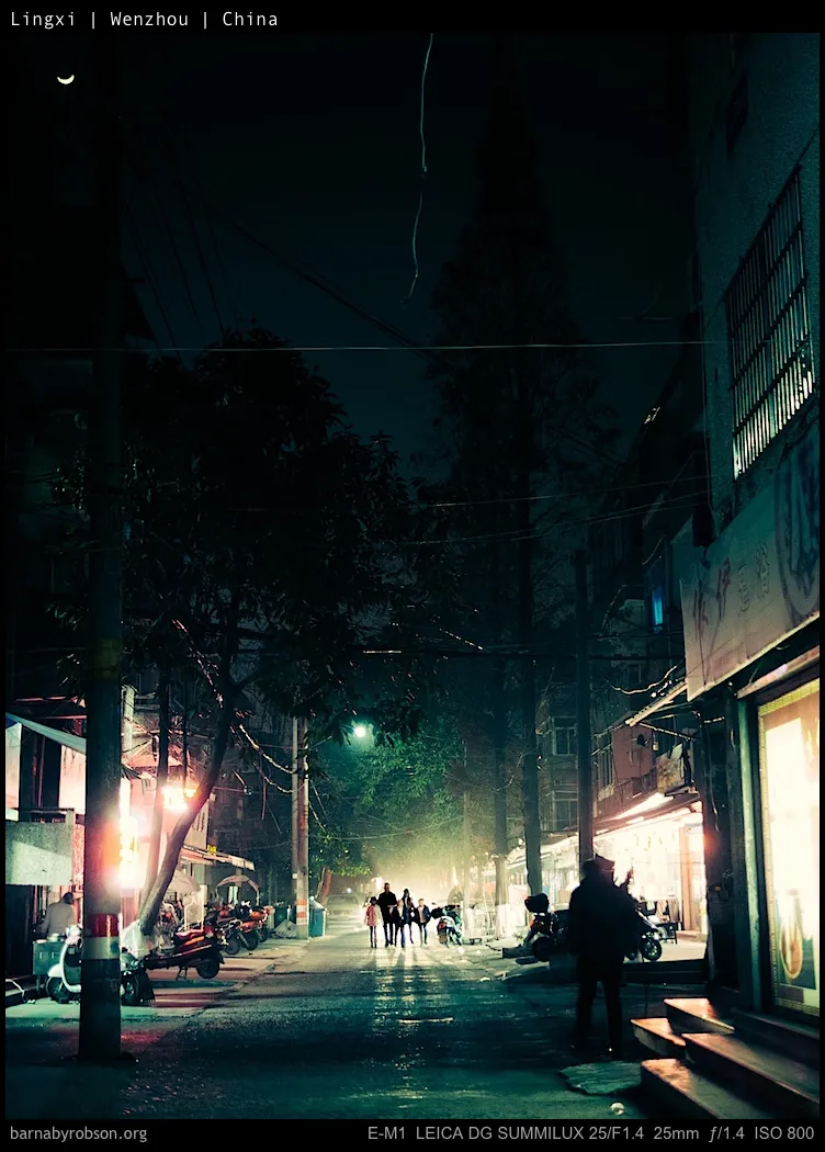 Night street, people walking on wet ground, reflecting lights, crescent moon.