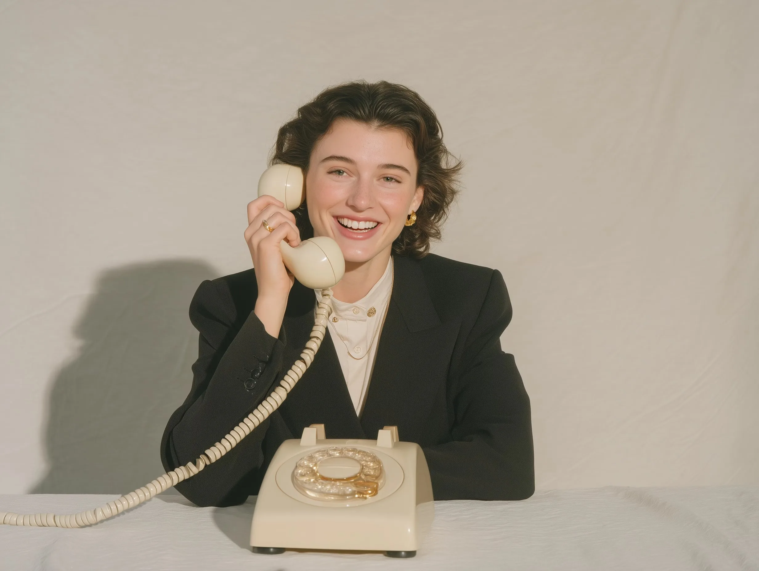 A woman in a blazer taking a call on a vintage telephone