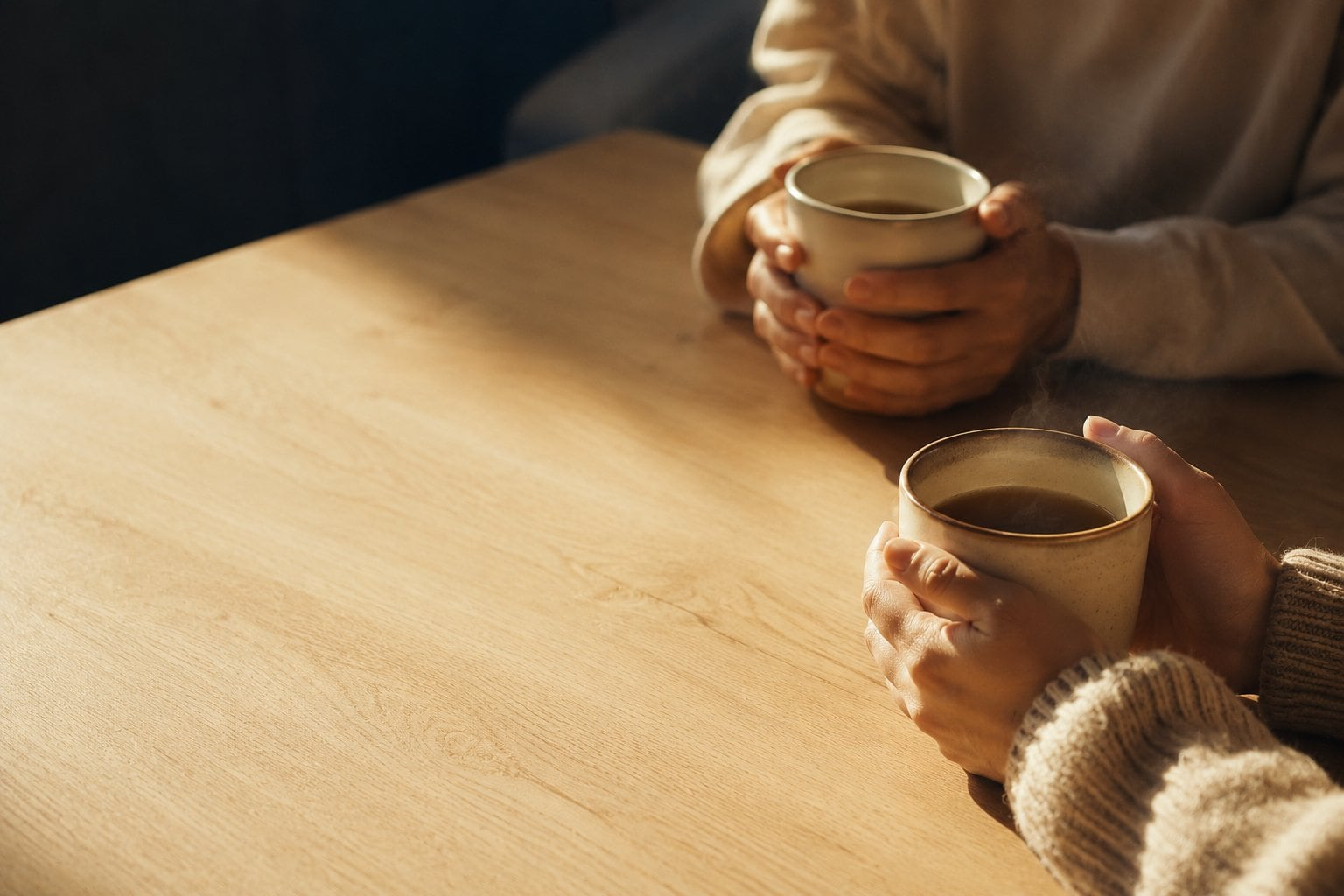 Two people sharing an unhurried break together, hands cupped around warm mugs