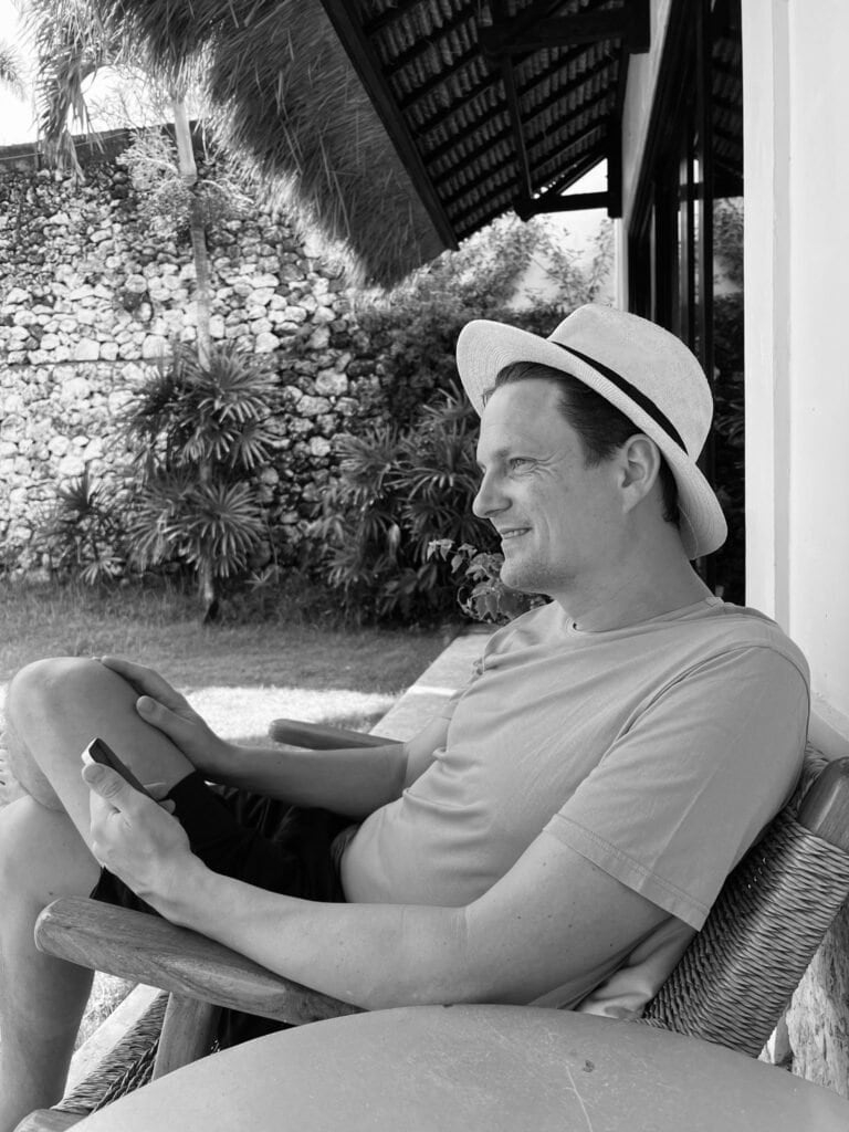 Barnaby Robson on a veranda in Indonesia, wearing a panama hat