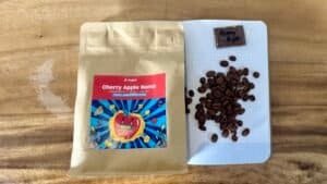 Rich roasted coffee beans and Cherry Apple Bomb seed packet on a wooden surface; perfect for coffee and gardening enthusiasts.