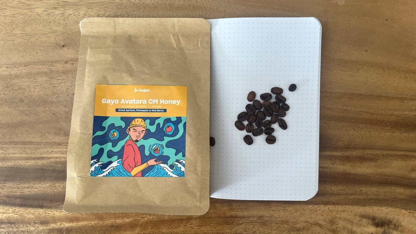Rich coffee beans on a white dotted tray next to a package of Gayo Avatara CM Honey coffee with a colourful illustration, ideal for specialty coffee and high-quality Arabica beans.