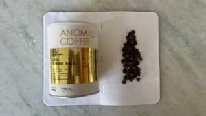 Rich Indonesian coffee beans on a dotted notebook with Anomali Coffee tin, showcasing premium Java Gunung Halu coffee for espresso enthusiasts and coffee connoisseurs.
