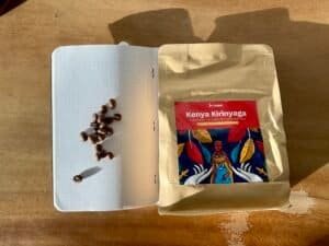 Realistic photo of Kenyan coffee beans on a notebook page with a bag of Kenyan Kirinyaga coffee on a wooden surface, highlighting premium coffee sourcing and quality beans.