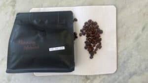 Flash roasted coffee beans on a dotted notebook next to a black sealed bag labelled "Puntang Natural" with a date label for January 25th.