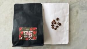 Rich coffee beans on dotted notebook page with black packaging labelled "Strawberry Fields" from Space Roastery, ideal for speciality coffee lovers and online coffee shop branding.