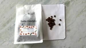 Fresh coffee beans and a coffee packaging bag from Hana Roastery, highlighting premium specialty coffee for roasting and brewing.