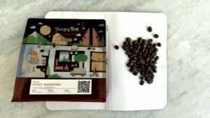 Rich coffee beans on dotted notebook page beside colorful coffee farm map, showcasing premium East Java Suket Mountain coffee, perfect for coffee enthusiasts and lovers of specialty coffee in the UK.