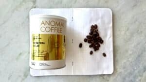 Roasted Sumatran coffee beans and a branded coffee tin on an open notebook, showcasing premium Indonesian coffee quality and specialty coffee beans for coffee lovers.