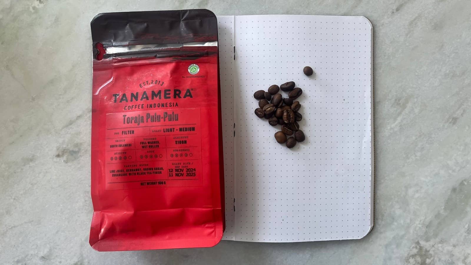 Rich coffee beans and Tanamera Indonesian coffee packaging on a dotted notebook, highlighting premium single-origin coffee, Indonesian brew, and coffee beans for brewing enthusiasts.
