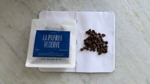 Pressed coffee beans on notebook with a bag of coffee labelled "La Papaya Reserve" for premium coffee beans and sustainable sourcing.
