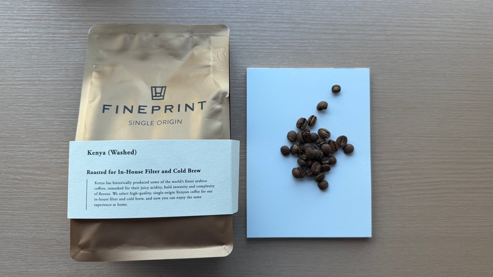 Close-up of roasted Kenyan coffee beans on a blue background with a bag of Fineprint single origin coffee. Perfect for coffee lovers and specialty coffee enthusiasts.