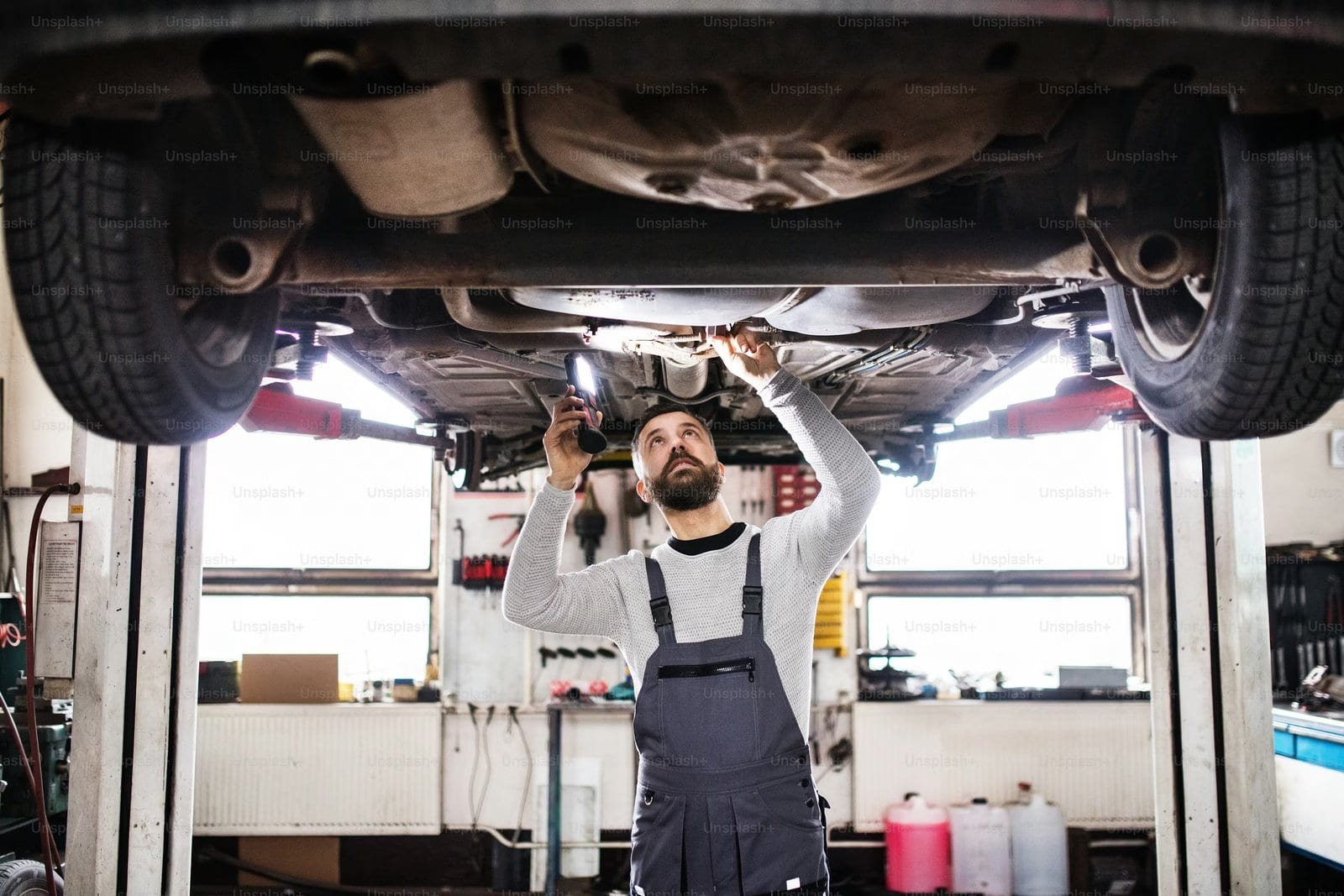 Skilled mechanic examining the undercarriage of a car lifted on a hydraulic lift in an auto repair shop, ensuring vehicle safety and maintenance.