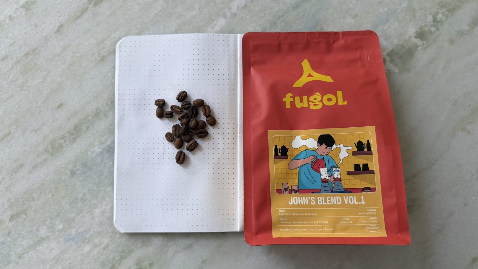 Fresh coffee beans next to a FUGOL coffee bag on a notebook, highlighting premium coffee products.