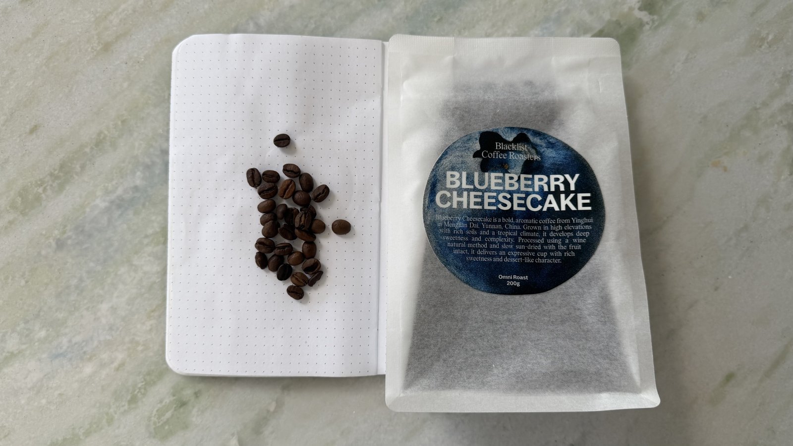 Freshly roasted blueberry cheesecake-flavored coffee beans on white paper with packaging, ideal for coffee enthusiasts and gourmet food lovers.
