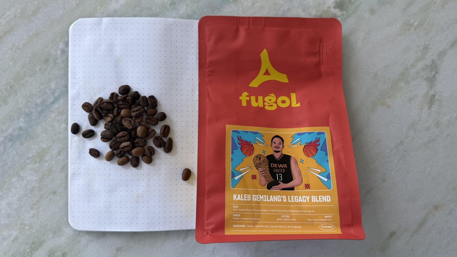 Bag of Kaleg Gentiang's Legacy Blend coffee with roasted beans on a white notebook.