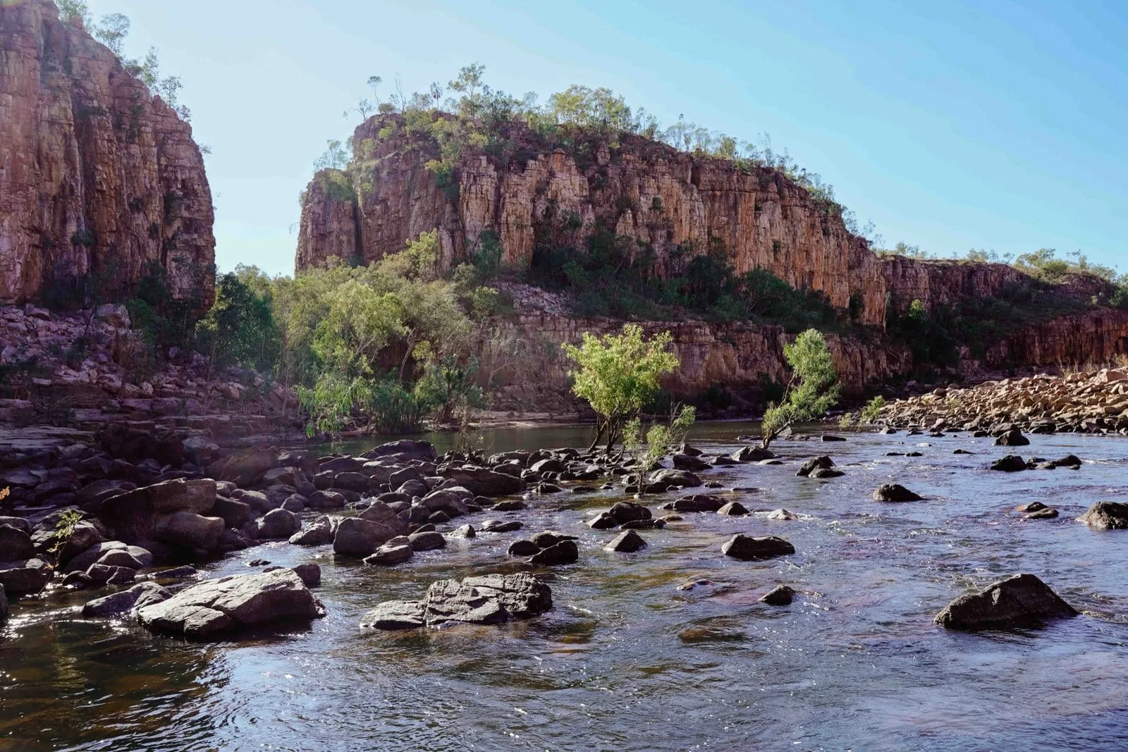 A shallow river winding between sandstone cliffs in Nitmiluk Gorge.